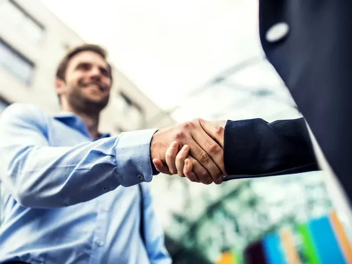 Two businessmen shaking hands outside modern office buildings, symbolizing successful partnership and trust
